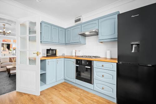 uma cozinha com armários azuis e um frigorífico preto em Luxurious 3 Bedroom House with Parking 73B - Top Rated - Netflix - Wifi - Smart TV em Holly Lane