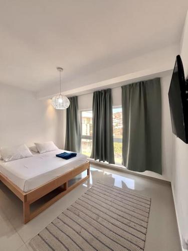 een witte slaapkamer met een bed en een televisie bij Bliss Apartments T1 - Madalena in Mindelo