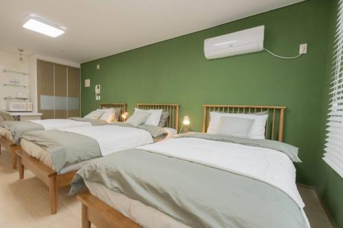 três camas num quarto com uma parede verde em MIRAE_stay 52 New Open [1 Queen + 2 Single beds] em Seul