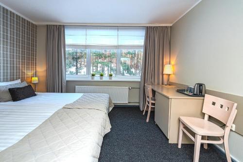 a hotel room with a bed and a desk and a window at Nykščio Namai & SPA in Anykščiai