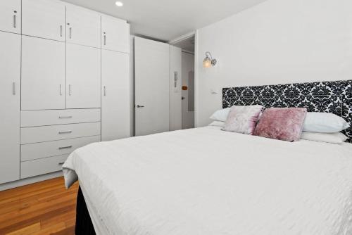 een witte slaapkamer met een groot wit bed met roze kussens bij Convenient Apartment in heart of Carlton in Melbourne