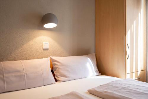 a bed with white sheets and a light on the wall at Antares Spiekerooger Gästehaus-Sonnengartenbalkon Nord - Wohnung 5 in Spiekeroog