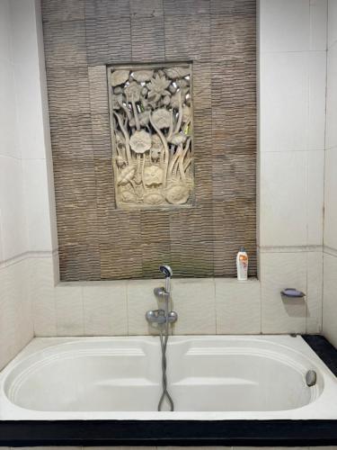 a bath tub in a bathroom with a painting on the wall at Nua House in Ubud