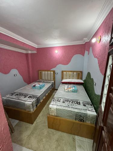 2 letti in una camera con pareti rosa di غرفه خاصه لك جديده وفرش جديد ومميز بها سريرين وتلفزيون a Mansoura