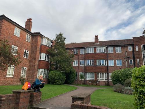 uma mulher sentada numa parede em frente a um edifício em Beddington Park Lodge West em Wallington