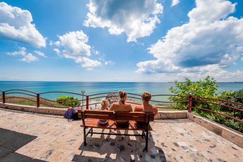 three people sitting on a bench looking at the ocean at Panorama Fort Beach in Sveti Vlas
