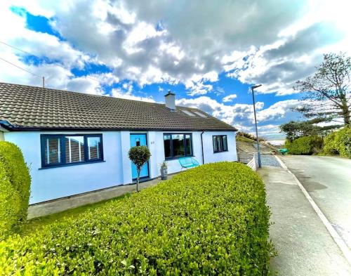 a white house with a green hedge in front of it at Bungalow, mountain and sea views parking in Aberdyfi