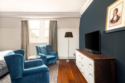a living room with two blue chairs and a television at Hotel Indigo - Edinburgh - Princes Street by IHG in Edinburgh
