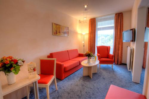 a living room with a red couch and two chairs at Hotel Hochsauerland 2010 in Willingen