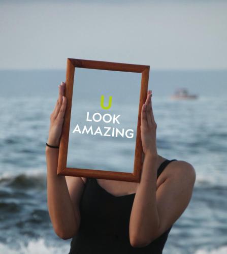 a woman sitting on the beach holding a sign that reads u look amazing at U11 Hotel & SPA in Tallinn