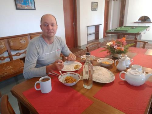 a man sitting at a table with a plate of food at Waterfield Bungalow by Liyozi Leasiure in Nuwara Eliya