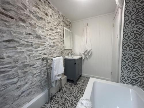 a bathroom with a stone wall and a sink and a tub at Little Cottage, Big Character in Pontypridd