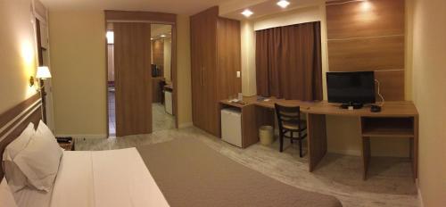 a hotel room with a bed and a desk with a television at Palace Hotel Campos dos Goytacazes in Campos dos Goytacazes