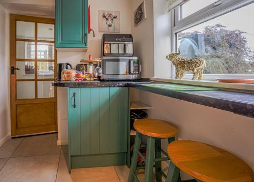 a kitchen with green cabinets and a counter with stools at Cosy cottage in rural Culmington, Ludlow in Culmington