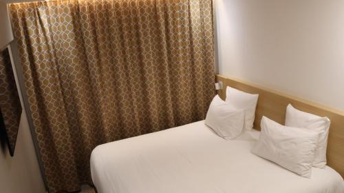 a bedroom with a bed with white sheets and pillows at Geographotel Paris-Roissy CDG Airport in Le Mesnil-Amelot