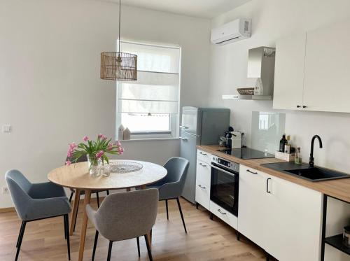 una cocina con mesa y sillas y una cocina con armarios blancos. en Pannonia Apartments en Mörbisch am See
