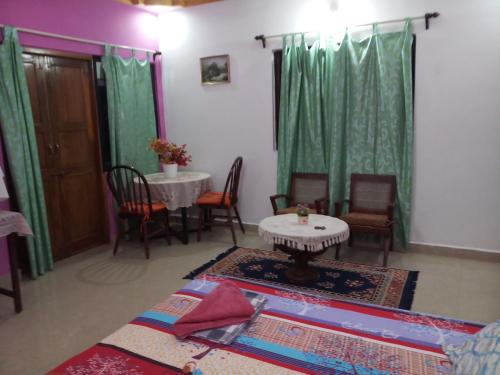 een woonkamer met een tafel en stoelen en groene gordijnen bij Casa Baptista Guest House in Goa