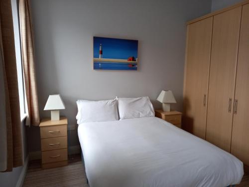 a bedroom with a white bed with two lamps and a painting at Town Square Holiday Homes in Lisdoonvarna