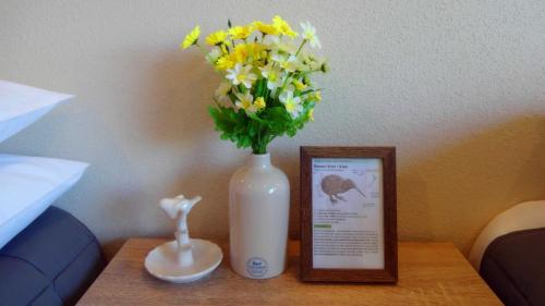 a white vase with flowers on a table with a picture at Rotorua Coachman Spa Motel in Rotorua