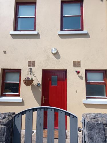 a building with a red door and a fence at Town Square Holiday Homes in Lisdoonvarna