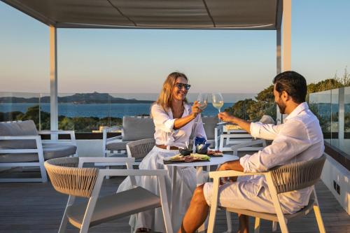 a man and woman sitting at a table with wine glasses at Hotel Grand Relais Dei Nuraghi in Baja Sardinia