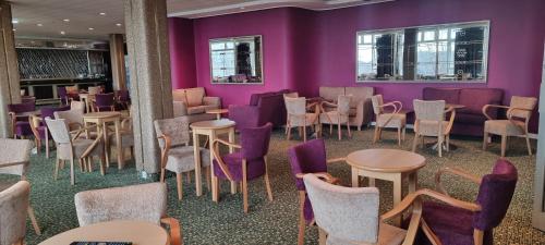 Shanklin Hotel في شانكلين: غرفة بجدران أرجوانية وطاولات وكراسي