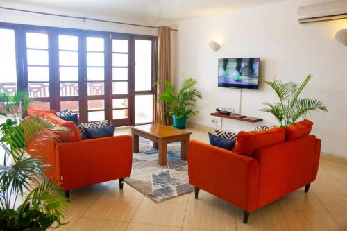 - un salon avec deux chaises orange et une télévision dans l'établissement Lux Suites Lamera Beachfront Apartments, à Shanzu