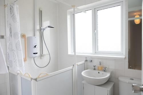 ein weißes Bad mit einer Dusche und einem Waschbecken in der Unterkunft Olivera House in Redruth