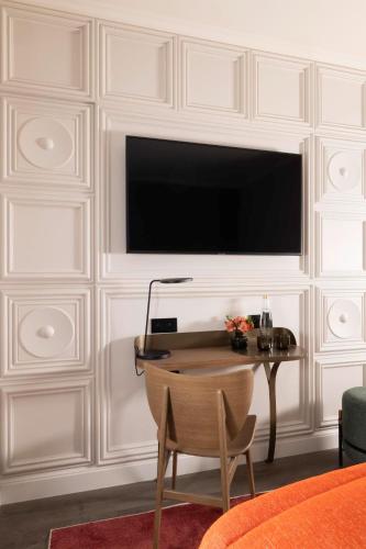 a living room with a table and a television on a wall at Hôtel L'Ormaie & Spa in Paris
