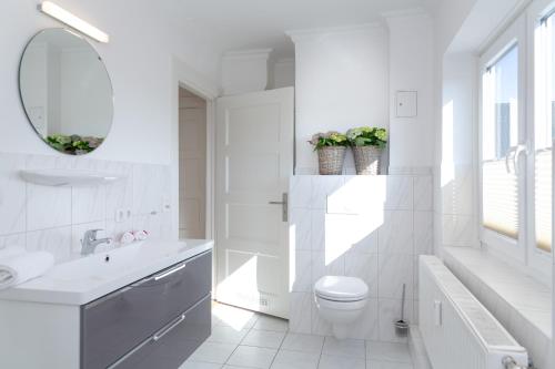 ein weißes Badezimmer mit einem Waschbecken, einem WC und einem Spiegel in der Unterkunft Inge-Marie in Westerland