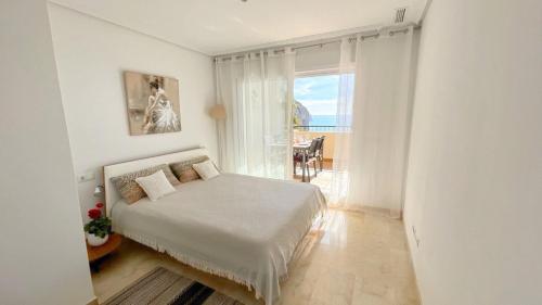 um quarto branco com uma cama e uma grande janela em Apartamento en Mascarat Beach, Urb Oasis Beach 1 em Altea