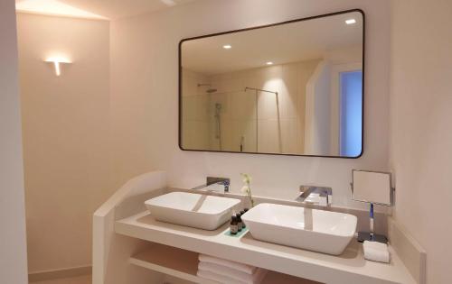 a bathroom with two sinks and a large mirror at Baia Di Chia Resort Sardinia, Curio Collection By Hilton in Chia