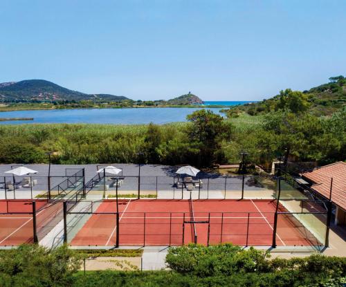 a tennis court with a lake in the background at Baia Di Chia Resort Sardinia, Curio Collection By Hilton in Chia