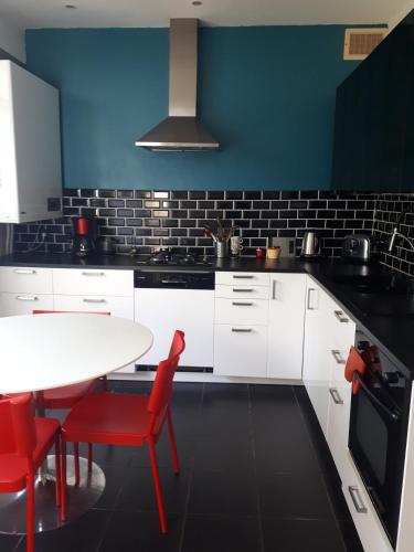 une cuisine avec des placards blancs et une table avec des chaises rouges dans l'établissement Maison T7, à Brest