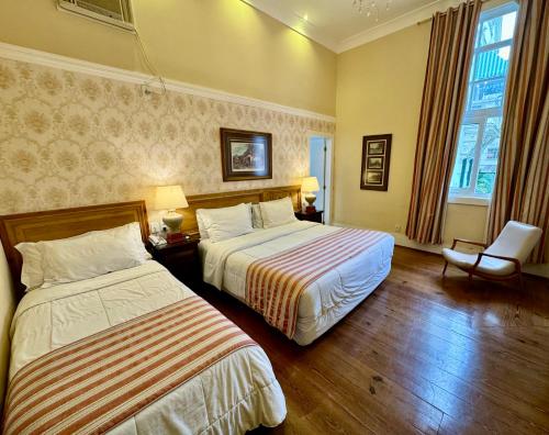 a hotel room with two beds and a chair at Hotel Casablanca Imperial in Petrópolis