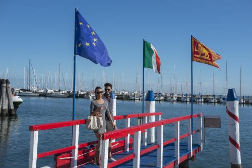 a man and a woman standing on a dock with flags at Hotel Grande Italia in Chioggia