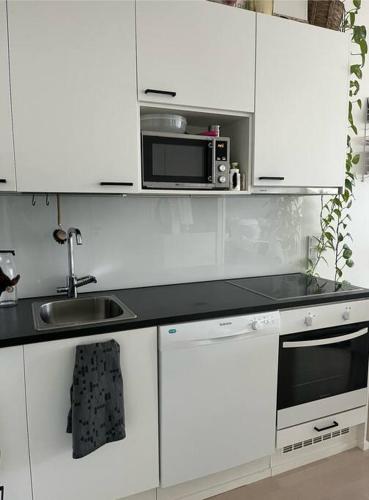 a white kitchen with a sink and a microwave at Modern apartment in great location in Vantaa