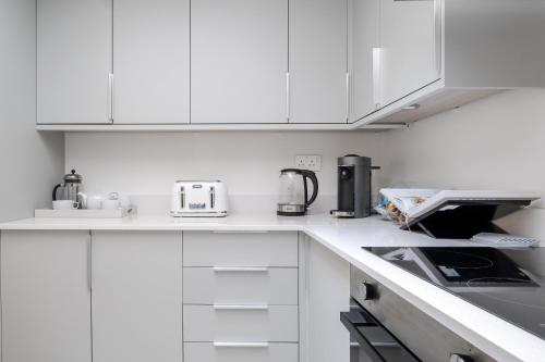 a white kitchen with white cabinets and appliances at Luxury Central Mayfair Townhouse with AC 3BR 3BA in London
