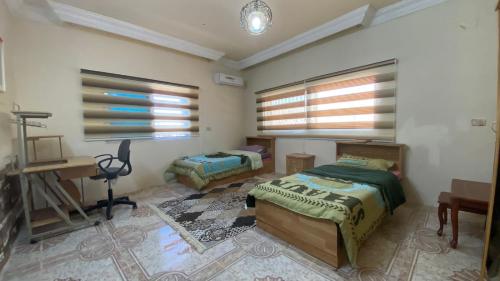 a bedroom with two beds and a desk and windows at فيلا في الطبيعة في عجلون in Ajloun