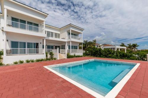 a villa with a swimming pool in front of a house at Breathtaking Turtle Tail Drive Oceanfront Villa in Providenciales