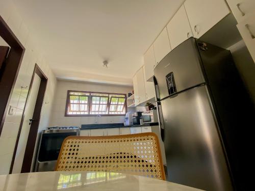 a kitchen with a table and a stainless steel refrigerator at Nossa Casa em Vilas - 70 m da areia - 6 Suítes in Lauro de Freitas