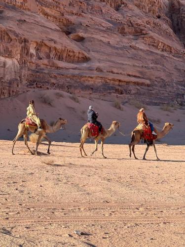 three people riding on camels in the desert at Scarlet Luxury Camp Wadi Rum in Wadi Rum