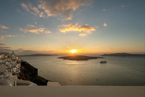 a sunset over a large body of water with a boat at Thera Villas in Fira