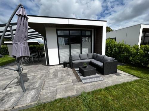 a patio with a couch and an umbrella in a yard at Ferienhaus / Chalet / Bungalow am See, Holland, Niederlande, Lathum in Lathum