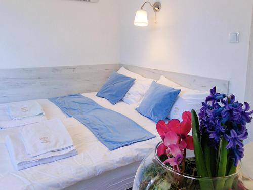 a bed with blue pillows and purple flowers in a vase at Pensjonat Alka in Kołobrzeg