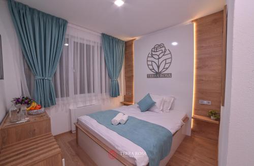 a small bedroom with a bed with blue curtains at Хотел Терра Роза in Karlovo