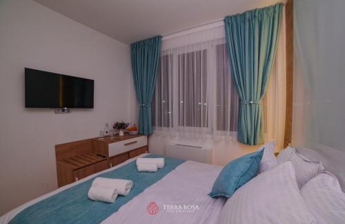 a bedroom with a bed with blue curtains and a television at Хотел Терра Роза in Karlovo