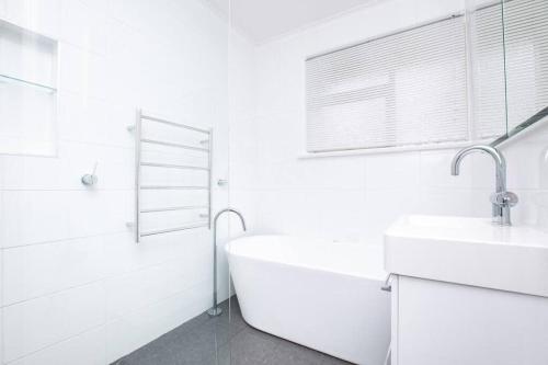 Baño blanco con bañera y lavamanos en Comfortable Home with Wifi Parking & Views, en Royal Park