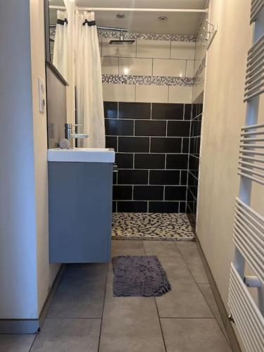 La salle de bains est pourvue d'un lavabo et d'une douche avec du carrelage noir. dans l'établissement Maison Téranga 2 Chambres Et 2 mezzanines et 2 parking gratuits, à Courrejean