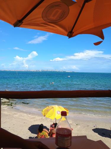 duas pessoas sentadas debaixo de um guarda-sol na praia em Pousada Villa do Mar em Itaparica